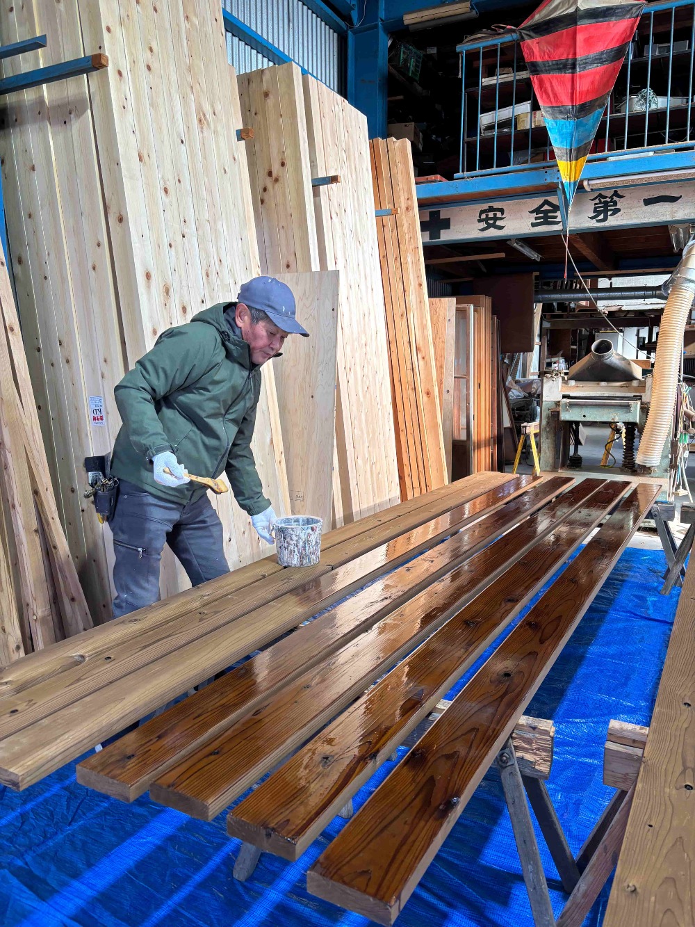 東濃桧の柱材を背に、 デッキ材を丁寧に塗装する川脇さん。  オスモを2回重ね、しっかりと保護していきます。